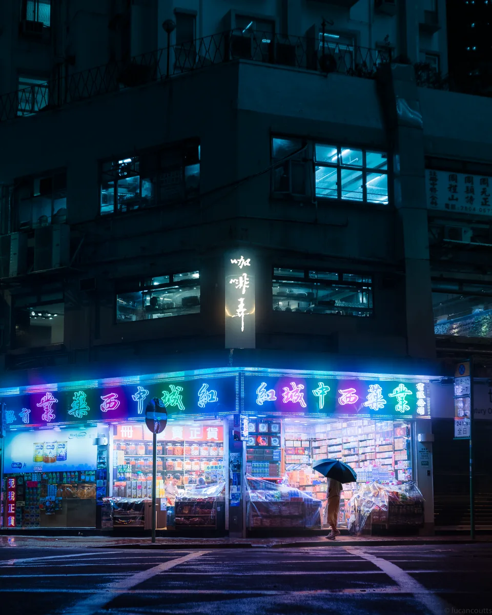 A neon-lit storefront in Causeway Bay, Hong Kong, with a figure under an umbrella outside