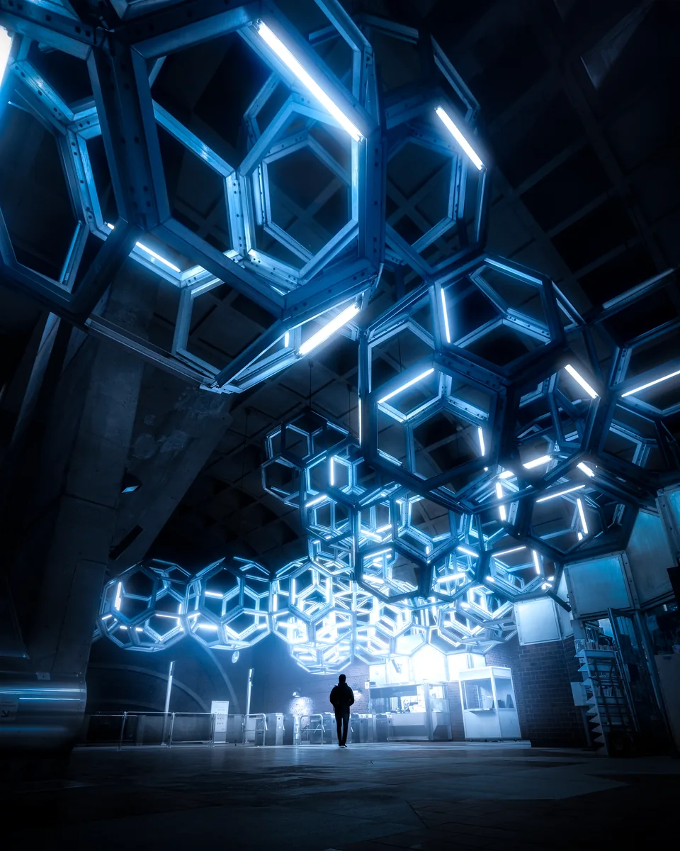 A small figure beneath a ceiling of glowing hexagonal light panels