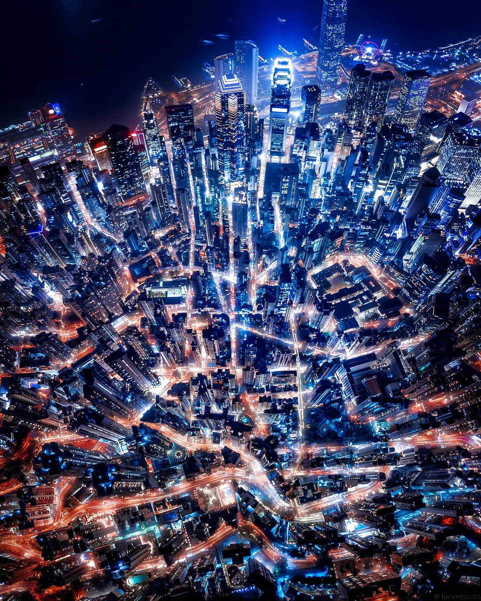 An aerial panorama of Hong Kong at night, a dense web of streets and towers lit in blue and orange
