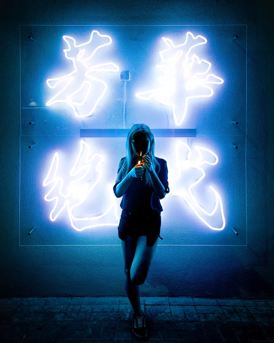 A woman in silhouette framed by a large blue neon sign in Hong Kong