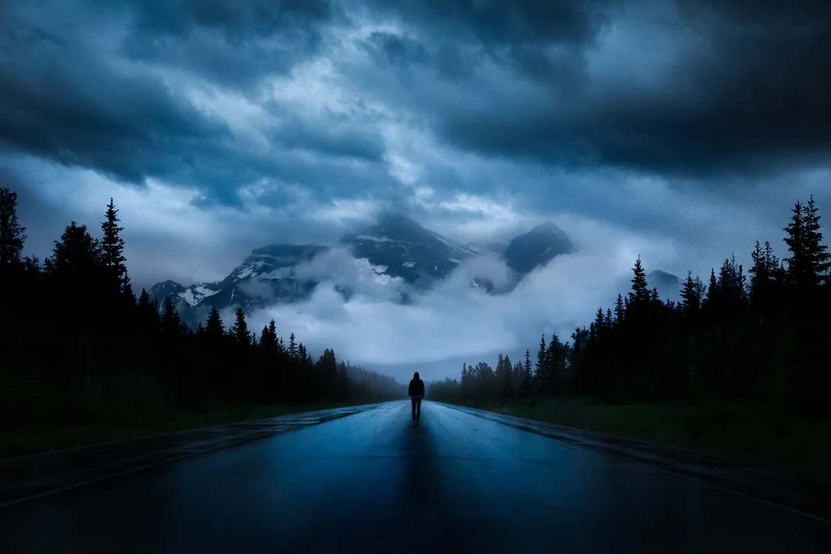 Icefields, a figure on an empty road leading toward storm-covered mountains on the Icefields Parkway, Alberta