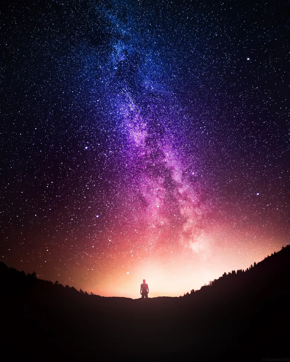 A composite of the Milky Way rising over a dark hill with a lone figure on the peak