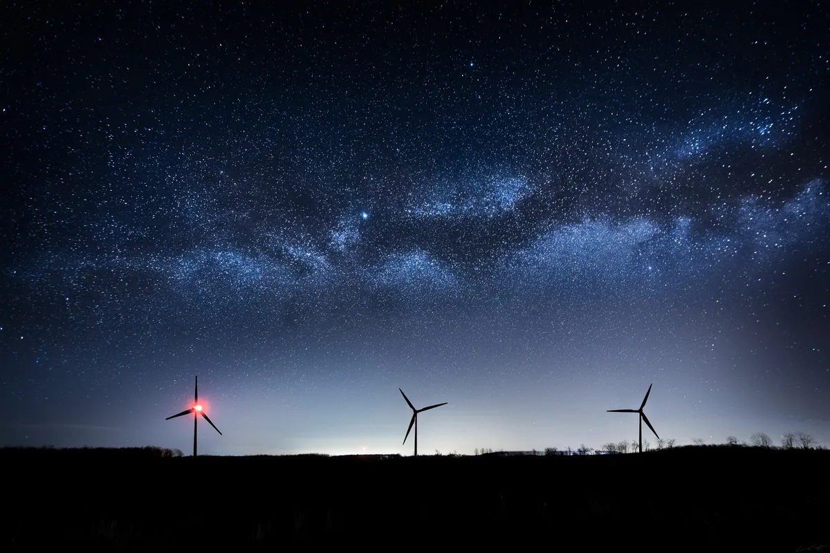 Sentinels, the Milky Way over a row of wind turbines with red lights in rural Ontario