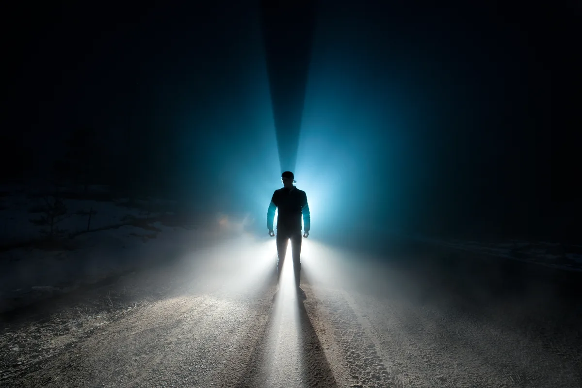 A figure silhouetted in a beam of light cutting through fog on a dark road in rural Ontario