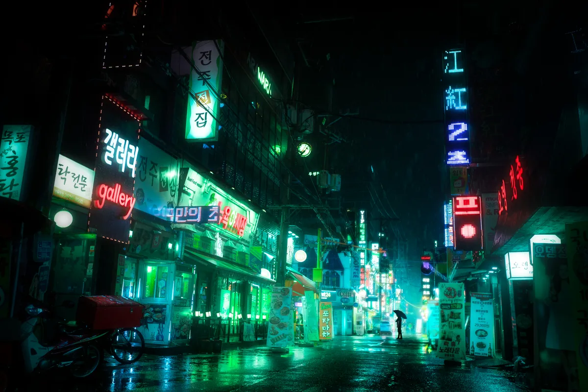 A narrow Seoul street at night lined with green and red neon signs